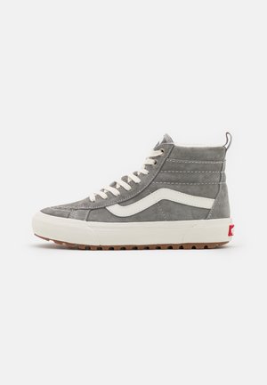 Sneaker grigio alta con striscia laterale bianca ondulata, lacci bianchi, colletto imbottito, suola bianca e suola esterna marrone scolpita su sfondo bianco.
