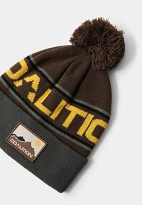 Brązowa dzianinowa czapka z pomponem na górze, z żółtymi i zielonymi paskami oraz napisem "KOALICJA". Obejmuje teksturowaną naszywkę logo.