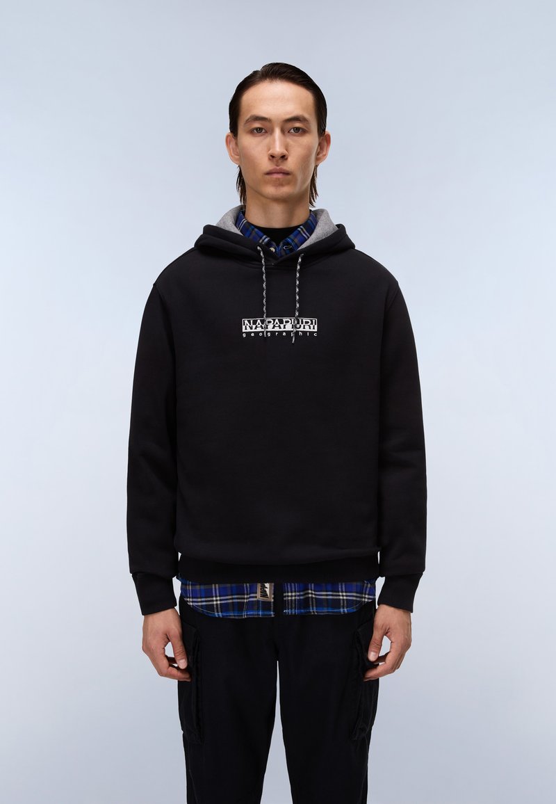 Felpa nera di cotone con fodera grigia, con un logo bianco centrato. Indossata sopra una camicia a quadri blu, abbinata a pantaloni cargo scuri.