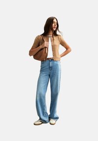 Cárdigan marrón de punto, top blanco, jeans de mezclilla azul holgados y zapatillas blancas. Bolso de hombro marrón con una textura suave y acentos de hardware sutiles.