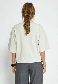 Light gray short-sleeve top with a relaxed fit, rounded neckline, and soft texture, paired with dark gray tailored pants.