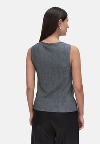 Grå, ribbad ärmlös topp med rundad halsringning, med en subtil textur och en knappdetalj bak. I kombination med svarta byxor.