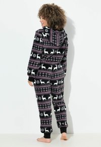 Conjunto de pijama de forro polar negro con capucha, que presenta patrones de renos y copos de nieve en blanco, acentuado con rayas rosas y moradas. Textura suave.