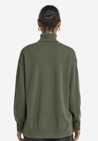 Übergroßer grüner Pullover mit hohem Kragen, gerippten Bündchen und Saum. Weiche Textur, mit herunterhängenden Schultern und einer lockeren Passform.