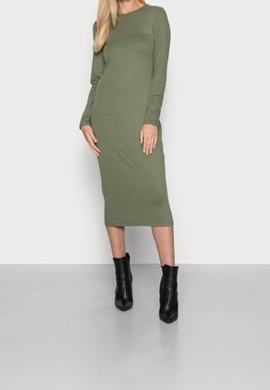 Olijfgroene, aansluitende midi-jurk met lange mouwen van zachte stof. Gecombineerd met zwarte enkellaarzen met een spits toelopende neus en een gestructureerde afwerking.