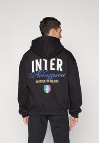 Sweatshirt preta com grandes letras brancas a dizer "INTER", com "Nerazzurri" em azul. Os detalhes incluem um escudo gráfico com "20" e cores italianas.