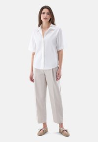 Weißes Kurzarmhemd mit Knöpfen und Kragen, kombiniert mit beigen, weit geschnittenen Hosen und hellbraunen Slippern mit einer Schleifenverzierung.