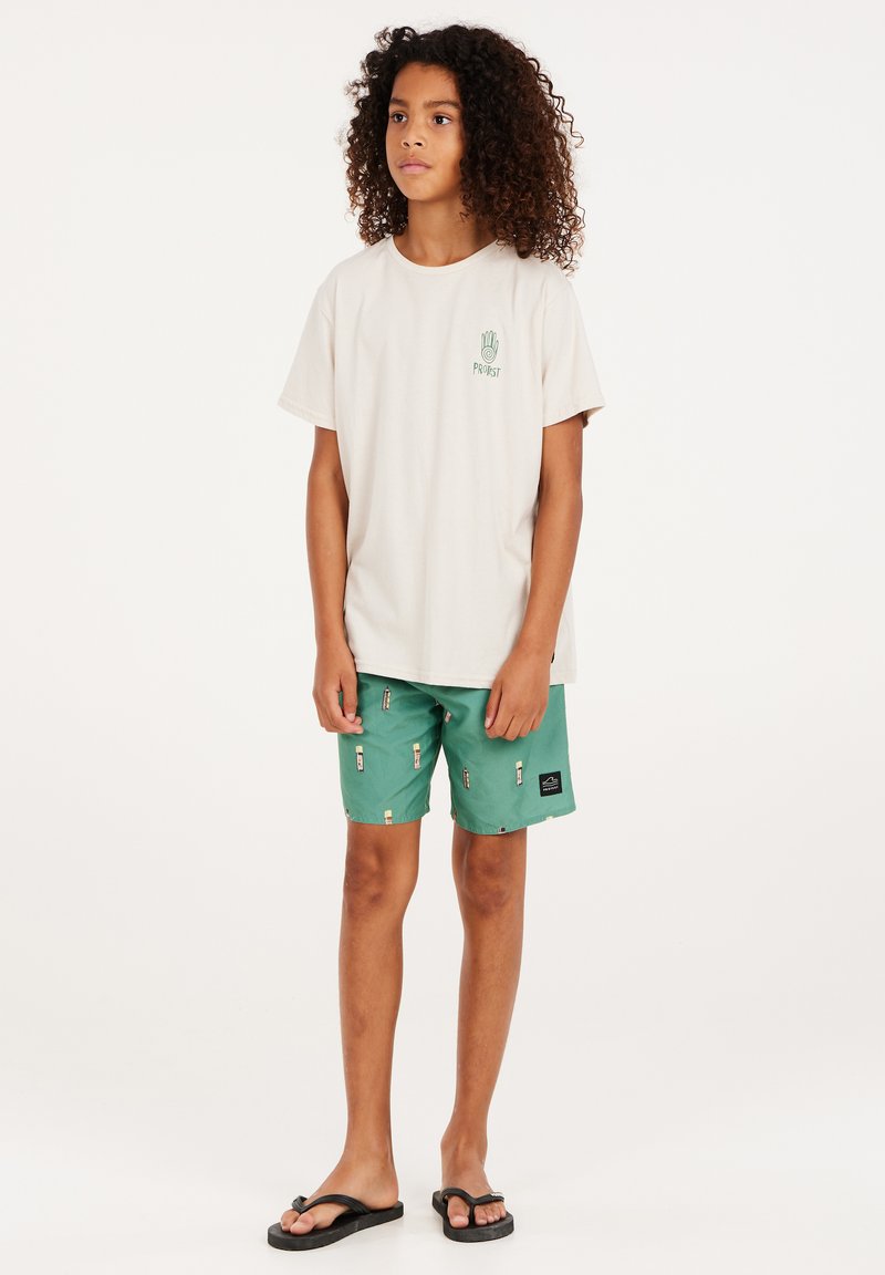 Lichtbeige t-shirt met groen logo, gecombineerd met groene shorts met een kleine print. Zwarte slippers maken de outfit compleet.