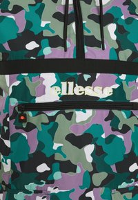Veste camouflage verte, violette, noire et blanche avec fermeture éclair noire et cordons, avec le logo jaune "ellesse" au-dessus de la fermeture éclair de la poche avant.