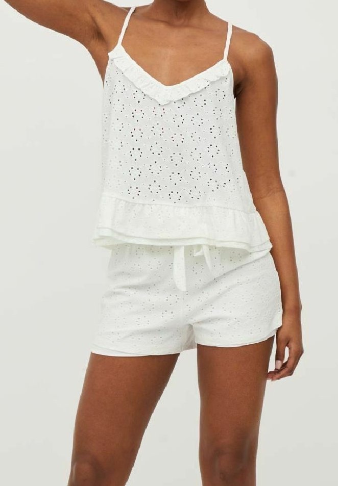 Set in cotone bianco composto da due pezzi, con top smanicato arricchito da dettagli in pizzo e pantaloni corti abbinati con vita regolabile tramite cordoncino.