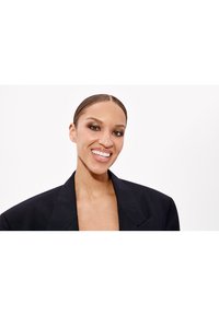 Sort oversized blazer med skarpe revers, i et struktureret stof. Emnet har lige, slicked-back hår og et strålende smil.