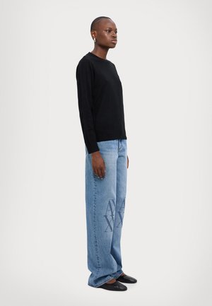 Maglione nero in maglia, jeans a gamba larga azzurri con motivo a logo e scarpe slip-on nere. Texture liscia con una vestibilità rilassata.