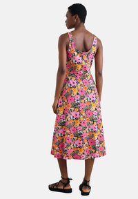 Robe florale avec un fond noir, présentant des fleurs roses, orange et blanches. Longueur midi, design sans manches, tissu lisse et taille cintrée.