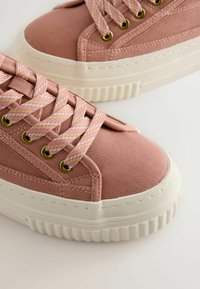 Rožiniai drobiniai sportbačiai su tekstūruota medžiaga, apvalia nosimi, balto gumos pado ir metaliniais akutėmis. Yra rožinės ir auksinės pynimo raišteliai.