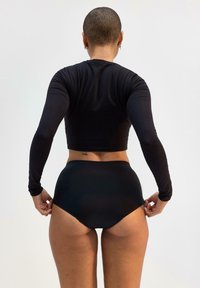 Svart långärmad crop top med en åtsittande design, i kombination med högmidjade svarta trosor. Slät textur och minimalistisk stil.
