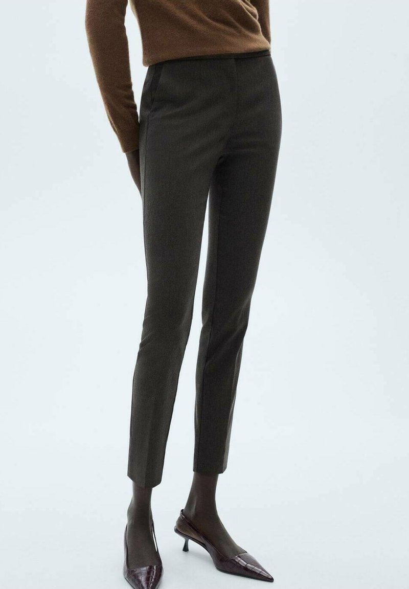 Personne portant un pantalon slim gris foncé longueur cheville, un haut marron à manches longues et des chaussures à talons kitten pointues de couleur sombre.