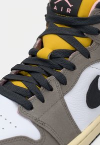 Close-up de um ténis cinza, branco e amarelo com cadarços pretos, mostrando o logótipo da Nike e a marca "Air" na língua.
