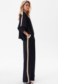 Zwarte tweedelige outfit met brede mouwen en rechte broekspijpen. Beige strepen accentueren de zijkanten. Gladde stof met een ontspannen pasvorm.