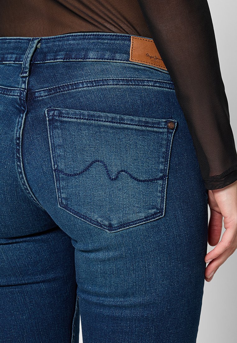 Jeans in denim blu scuro con una vestibilità slim, dotati di un'etichetta in pelle marrone sulla vita e un distintivo design a punto ondulato sulla tasca posteriore.