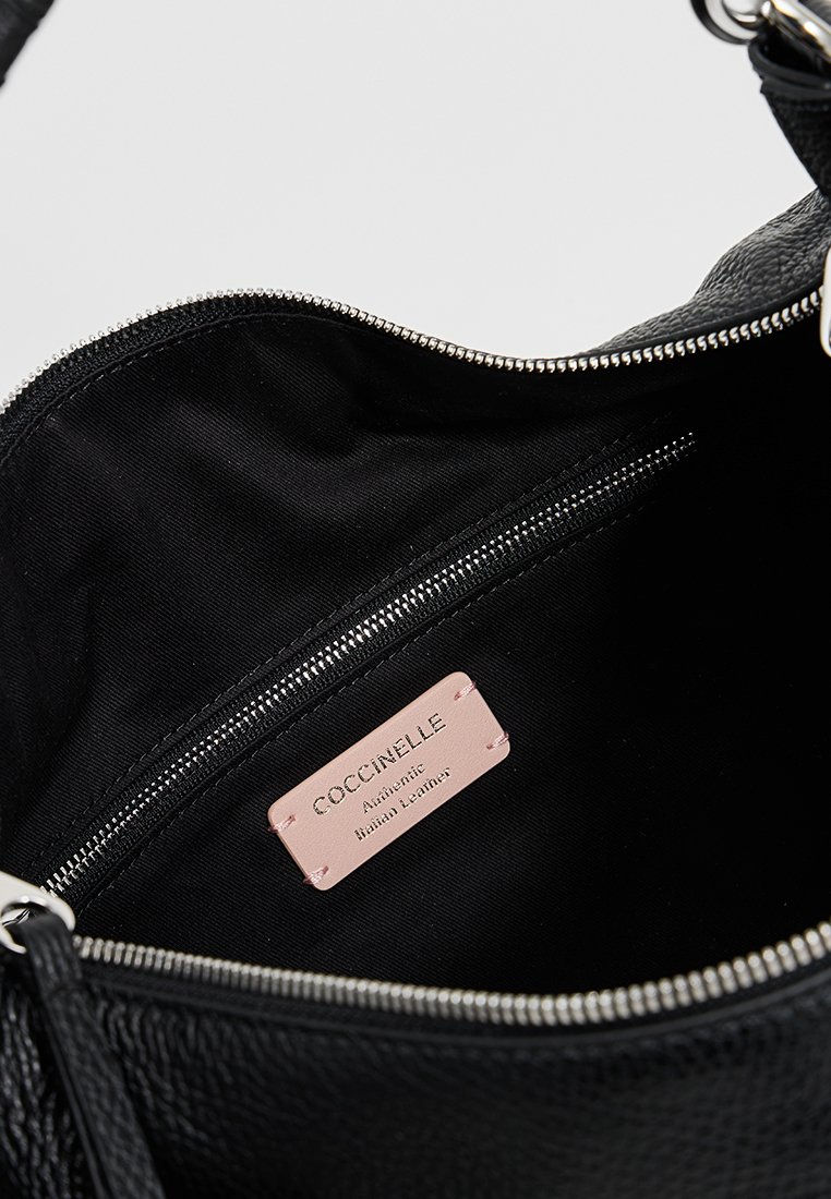Interno di una borsa a tracolla nera in pelle, dotata di una tasca con zip e un'etichetta rosa che recita "COCCINELLE Pelle Italiana Autentica."