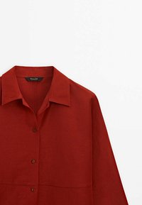 Chemise rouge à manches longues avec col et boutons marron sur le devant, présentée sur fond blanc.