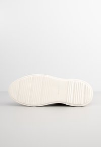 Weiße Gummisohle mit horizontalen Rillen für Grip, mit dem eingeprägten Markennamen "GANT" in der Nähe des Fersenbereichs.