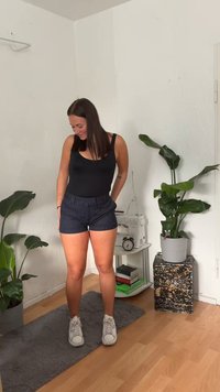 Svart body kombinerad med shorts i marinblått med ränder. Shorts har bälte, fickor och är skräddarsydda. Vita sneakers och en strukturerad grå matta syns.