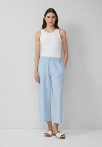 Pantalons bleu clair à coupe décontractée avec une taille élastique et des poches latérales, associés à un débardeur blanc et des sandales blanches.