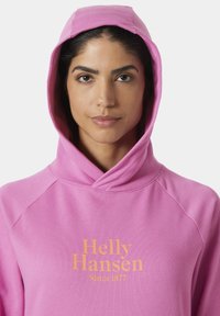 Sudadera rosa con corte relajado y capucha, con el logo "Helly Hansen" y "Desde 1877" en amarillo. Textura suave y mangas raglán.