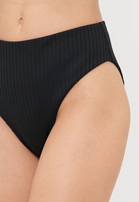 Hochgeschnittene schwarze Bikinihose mit vertikal gerippter Textur und mittlerem Beinausschnitt. Sie zeichnet sich durch eine glatte Oberfläche und einen elastischen Bund für zusätzlichen Komfort aus.