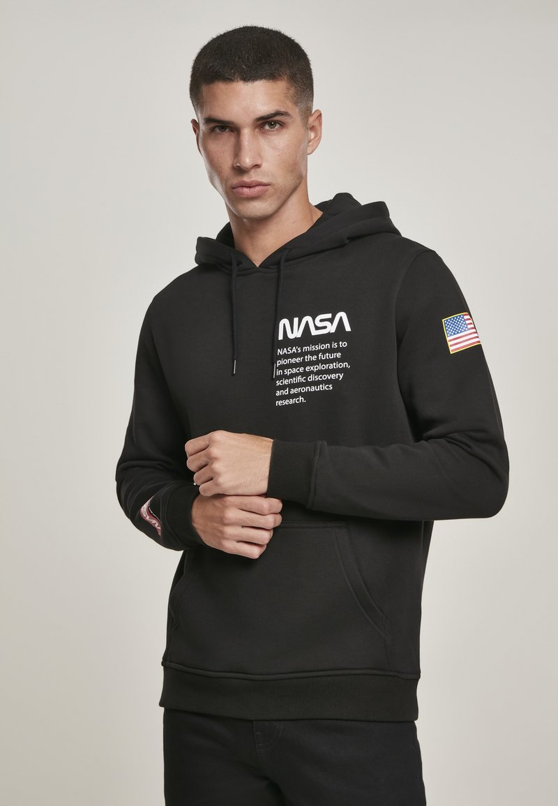 Un sweat à capuche noir avec le logo de la NASA et du texte de mission imprimé en blanc. Il possède une poche avant et un patch du drapeau américain sur la manche gauche.