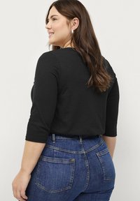 Top negro de manga 3/4 combinado con jeans de cintura alta azul oscuro. La tela parece suave con una textura lisa. Detalles de costura visibles en los jeans.