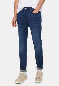 Dark blue jeans with a slim fit, made of denim, featuring five-pocket styling and rolled cuffs. Worn with beige sneakers.