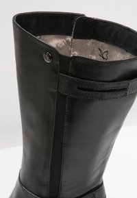 Black leather knee-high boot with a smooth finish, featuring a textured accent panel, elastic side, and metallic logo detail.