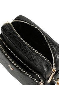 Černá kožená taška s texturovaným povrchem, dvojitými zipovými přihrádkami a akcenty zlatého kovu. Vnitřek je podšitý měkkou tkaninou.