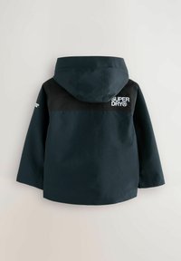 Mörkblå vattentät jacka med huva, med svart övre del och vitt "SUPERDRY"-logotyp på baksidan. Slät textur, avslappnad design.