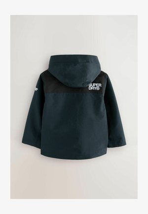 Námořnická modrá nepromokavá bunda s kapucí, s černou horní částí a bílým logem "SUPERDRY" na zadní straně. Hladký povrch, ležérní design.
