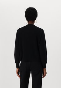 Svart strikket genser med dropped shoulders, ribbe-textur, rund hals og løs passform. Kombinert med svarte bukser, minimal detaljer.