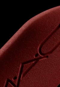 Red rubber insole featuring a smooth texture with raised line patterns and a subtle shine. Rounded shape, designed for foot comfort.