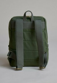 Mochila de tela verde con respaldo acolchado, dos correas ajustables, asa superior y detalle de cremallera en tono dorado. Superficie texturizada y forma estructurada.