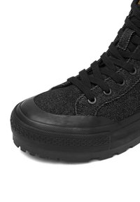 Melns augstais sporta apavs ar teksturētu auduma augšdaļu, gumiju pirkstu aizsargu un plānām melnām šņorēm. Zole ir ar rakstainu dizainu, lai nodrošinātu saķeri.