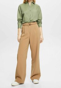 Camicia button-up verde chiaro con maniche lunghe abbinata a pantaloni beige a vita alta e gamba larga, insieme a sneaker bianche. Design semplice e lineare.