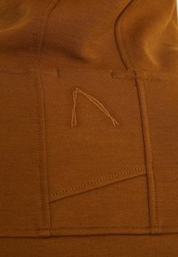 Gros plan d'un tissu marron avec des coutures visibles et un petit motif abstrait brodé dans un fil assorti.