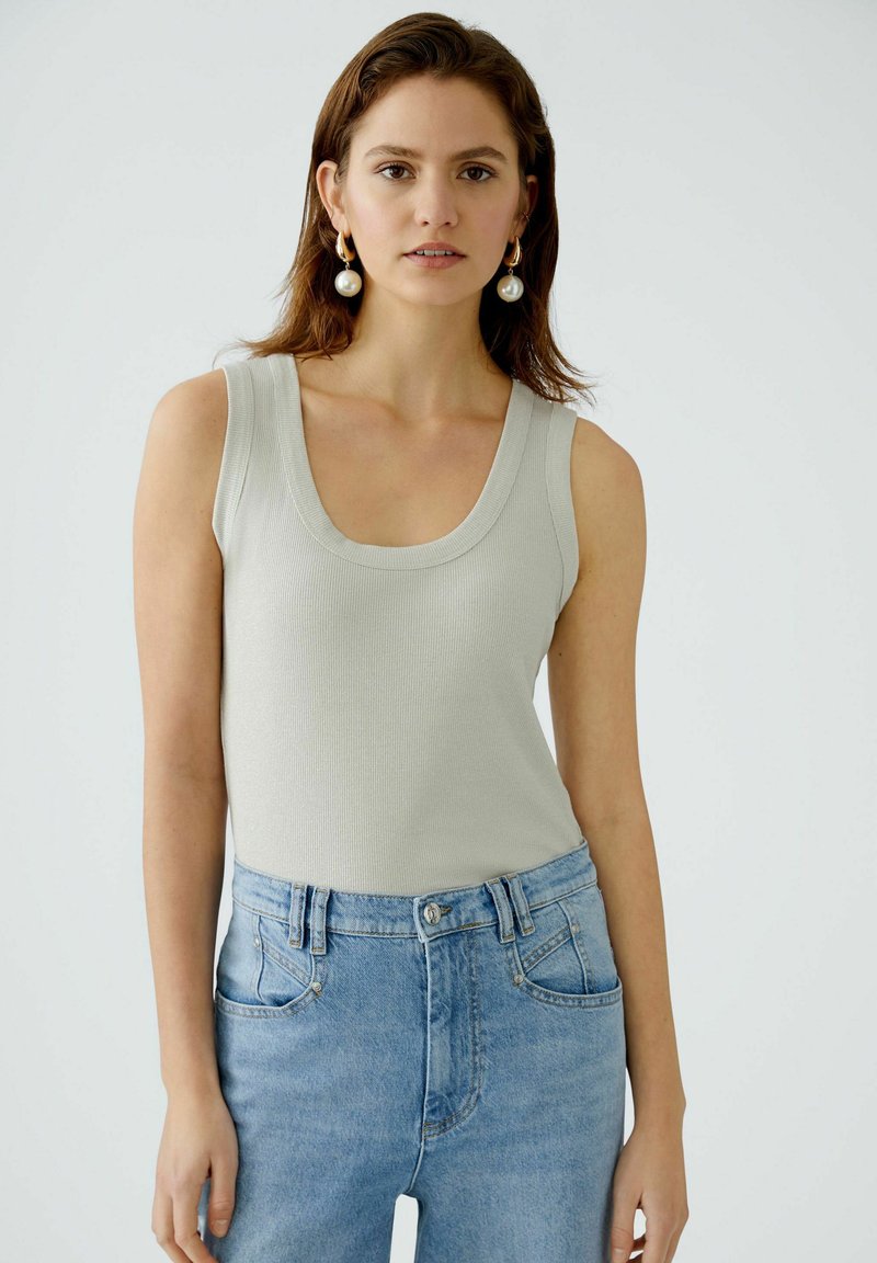 Light gray, ribbed tank top with a wide scoop neckline, paired with high-waisted light blue jeans featuring two front pockets and a button closure.