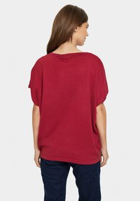 Haut rouge surdimensionné à manches courtes avec une texture côtelée. Coupe ample avec un col rond. Associé à un jean en denim foncé. Vue de dos.