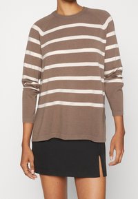 Pull rayé marron avec des rayures horizontales crème, col rond et manches longues. Associé à une mini-jupe noire avec une fente latérale.