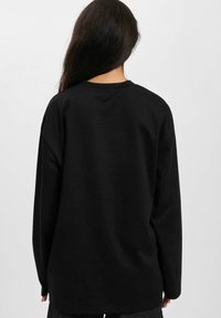 Black long-sleeve sweatshirt with a relaxed fit. Features a round neckline and smooth texture. Minimalist design; no visible patterns or accents.