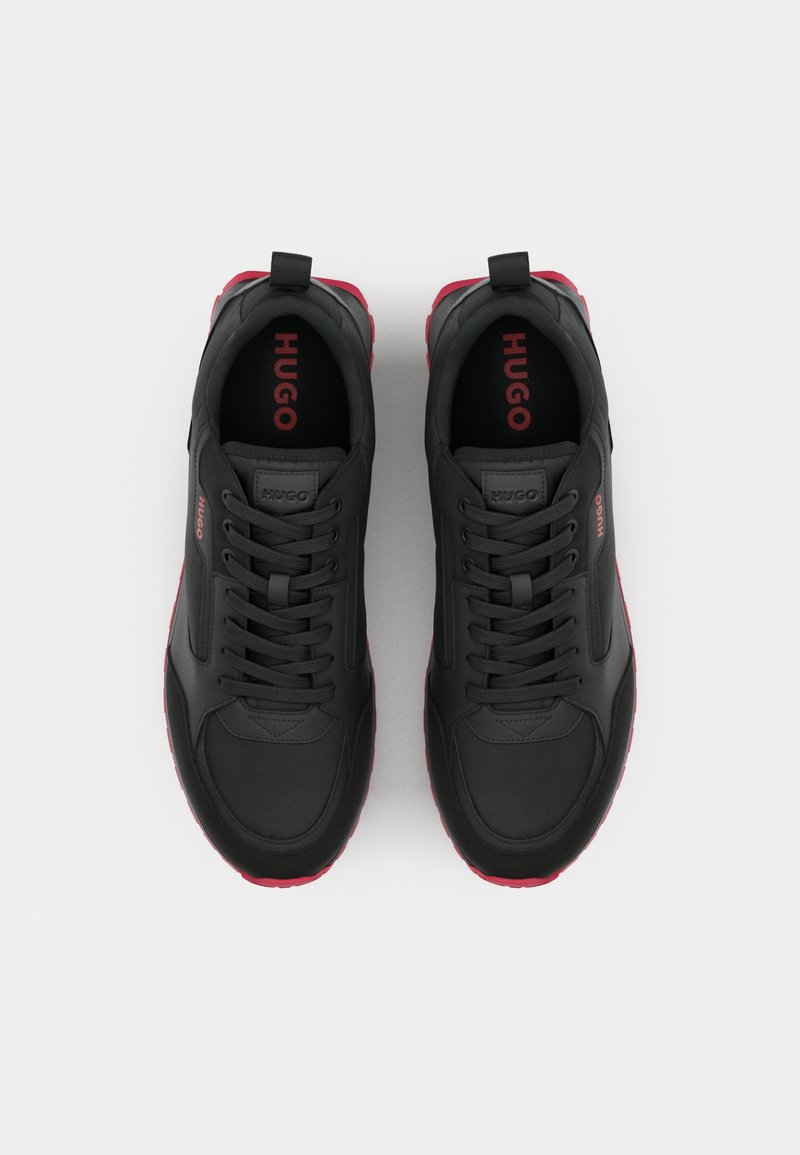 Scarpe sportive nere con accenti rossi, dotate di una tomaia in materiale sintetico liscio, lacci frontali, colletto imbottito e suola in gomma testurizzata.