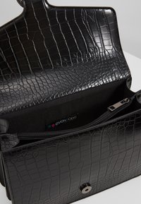 Schwarze Handtasche aus Kunstleder mit Krokodilprägung, ausgestattet mit einem Reißverschluss-Innenfach und einem Druckknopfverschluss für sichere Befestigung.