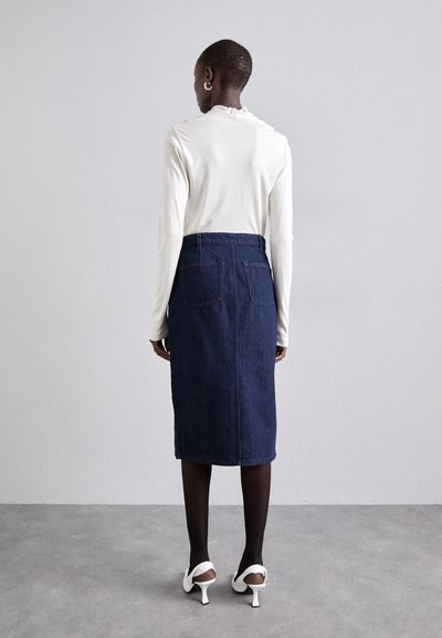 Crème kleurige lange mouwen top gecombineerd met een donkerblauwe denim kokerrok, voorzien van achterzakken en een getailleerde tailleband. Witte hakken maken de look compleet.